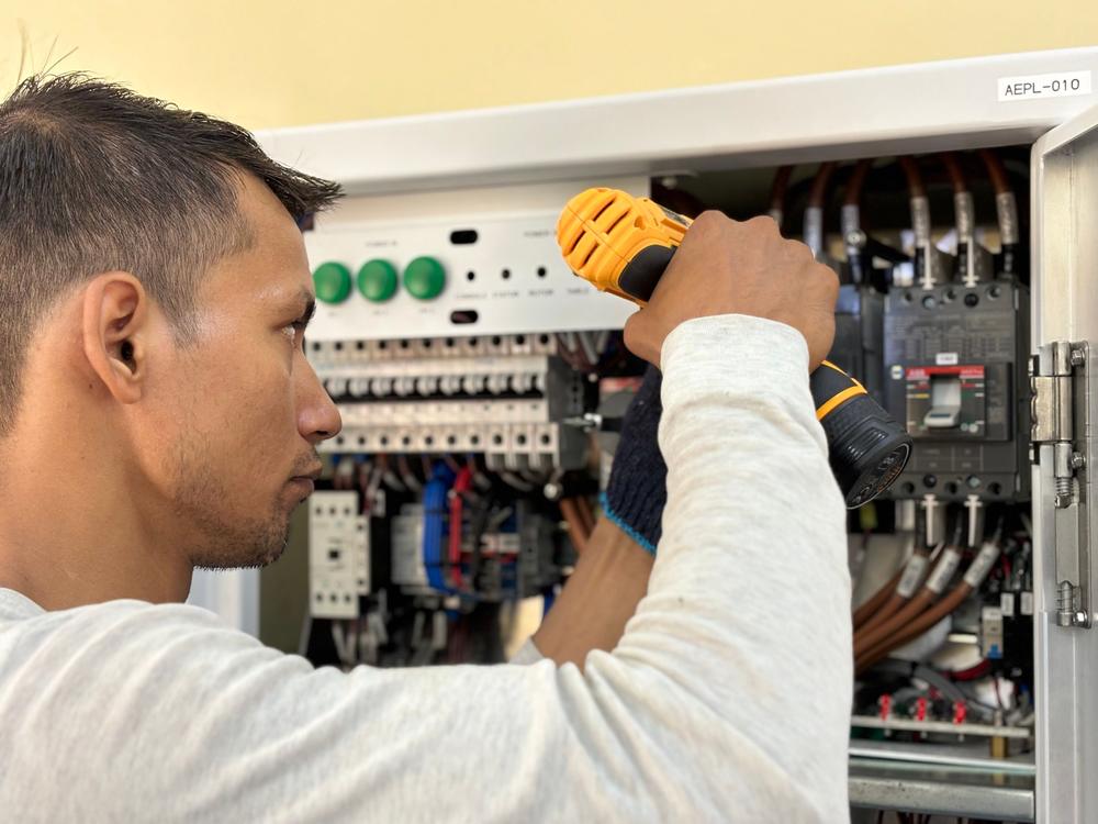 Électricien vissant un appareil dans un tableau électrique ouvert